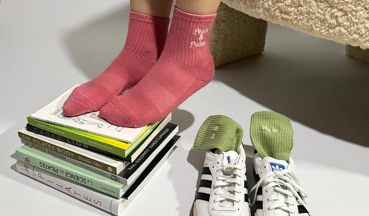 Person wearing pink non-slip Pilates socks, standing on a stack of books with green Pilates grip socks next to it