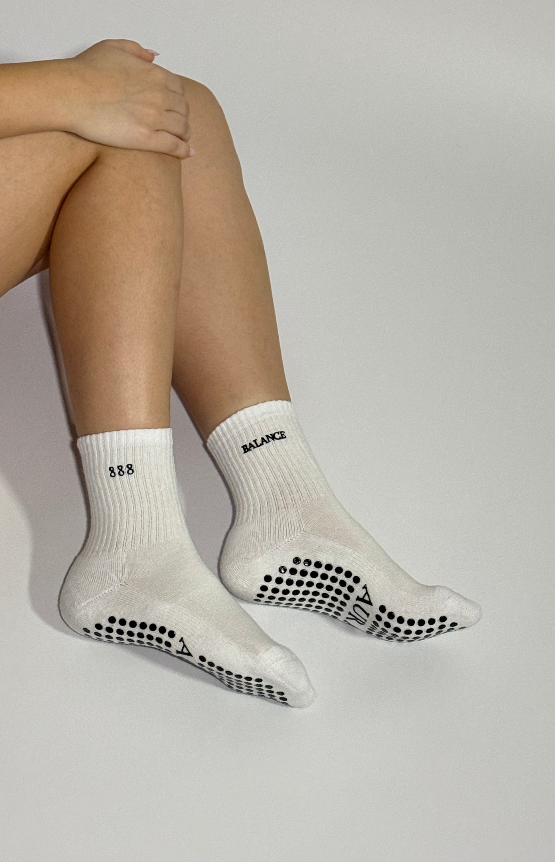 White 888 socks with black grip dots and AURA logo worn by a person on a light gray background
